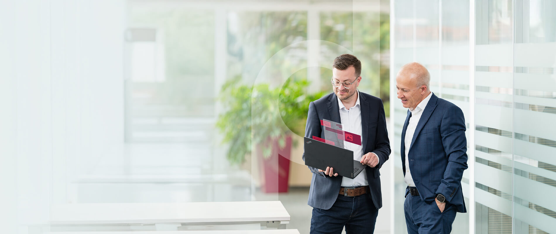 Two businessmen are standing in a modern office building, discussing something on a laptop with digital overlays.