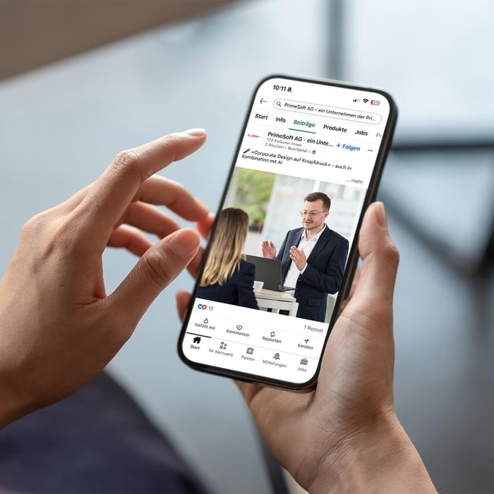 Two hands hold a smartphone displaying a LinkedIn post from PrimeSoft AG on its screen.