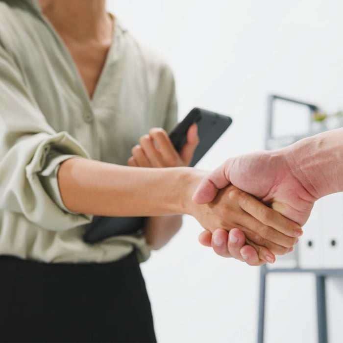 Close-up of a handshake between two business partners. The woman is holding a tablet.