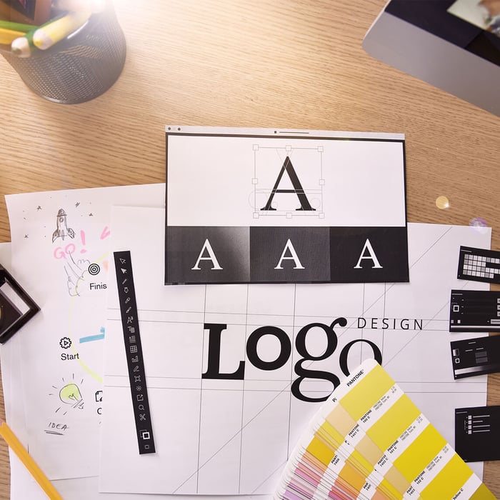 Top view of a desk with corporate design drafts on it, including a logo lettering and a color fan.