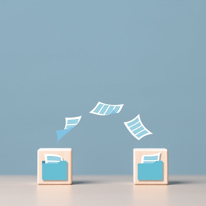 Two wooden blocks with folder icons, between which digital documents fly back and forth, symbolizing data transfer.
