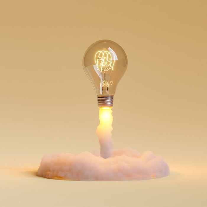 Glowing light bulb takes off like a rocket. A yellow flame leads to a white cloud.