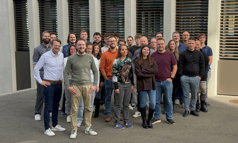Team photo of the PrimeSoft Group with over twenty smiling employees in front of an office building.