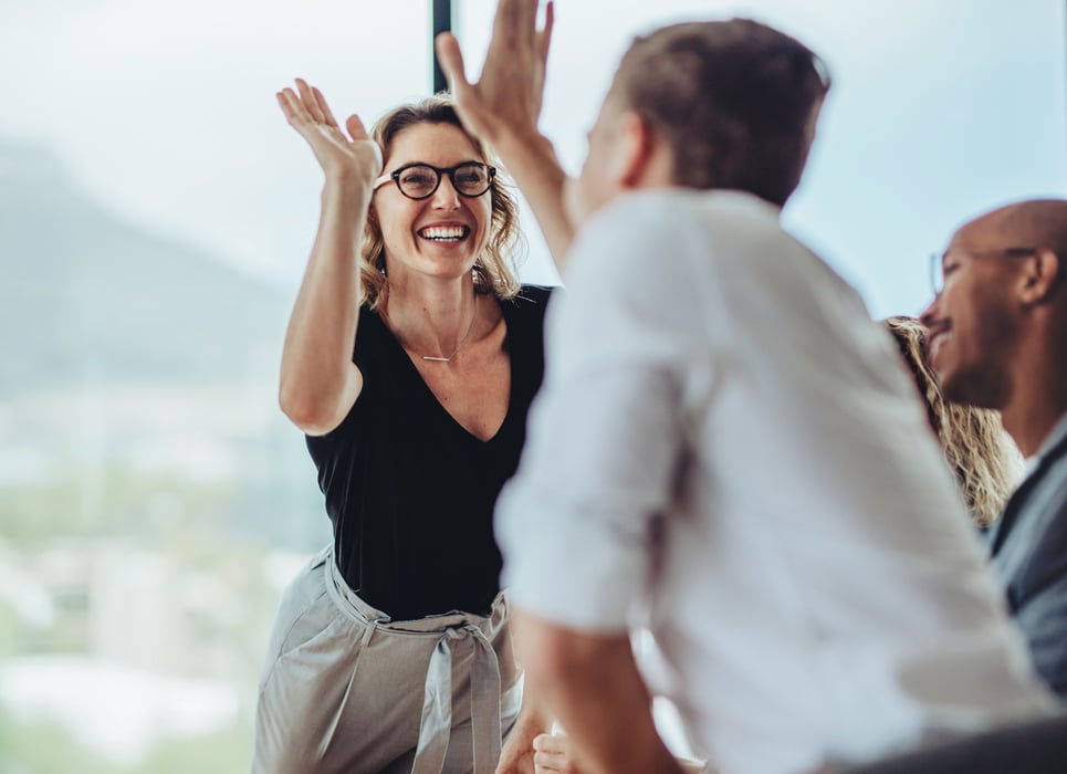 A smiling businesswoman gives a colleague a high five in a bright, modern office.
